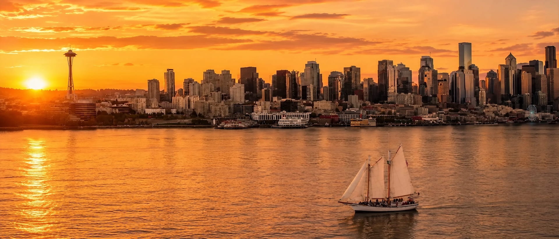 Tall-masted sailboat crossing Elliott Bay as the sun sets behind the Space Needle and downtown skyline on a Seattle sunset cruise