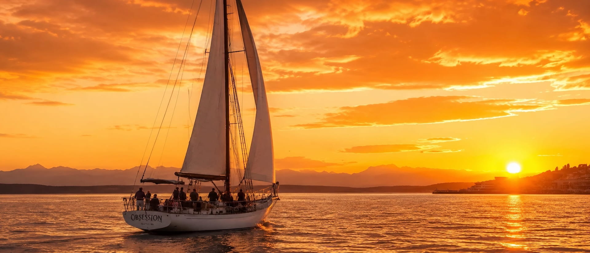 Two-masted schooner under full sail at sunset, the Olympic Mountains in silhouette behind it, sunset sailing in Seattle